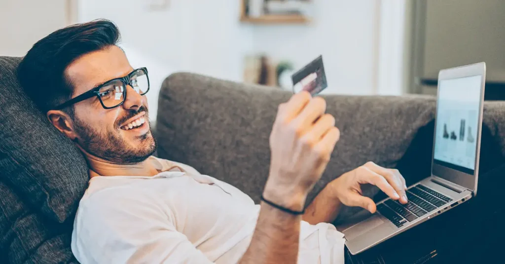 Man on couch with laptop reading credit card info