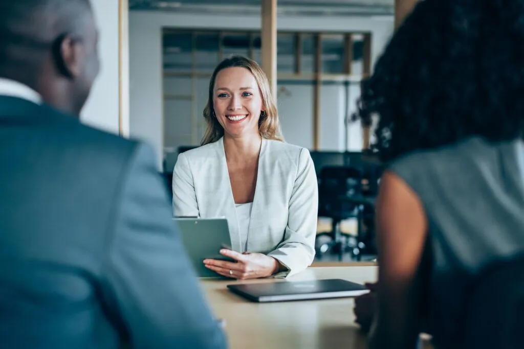 a woman sitting at a table holding a tablet and smiling