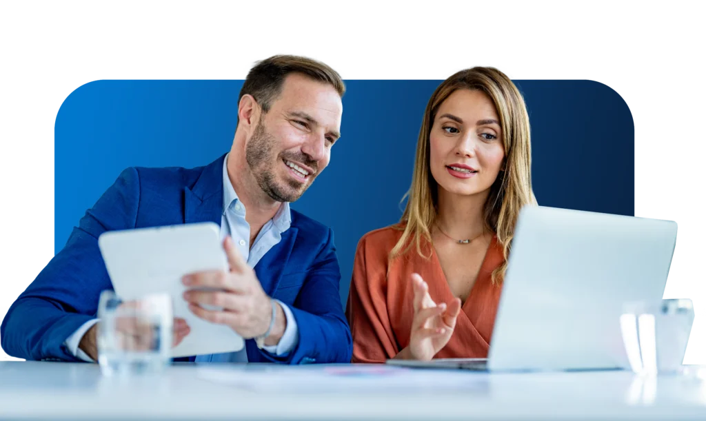 A photo of a man and a woman talking and working on their computers.