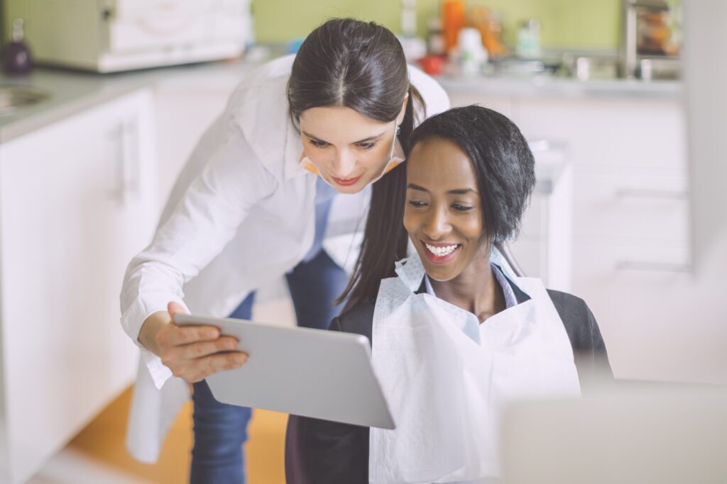 A dentist reviews patient information on a tablet with a patient in a dental chair