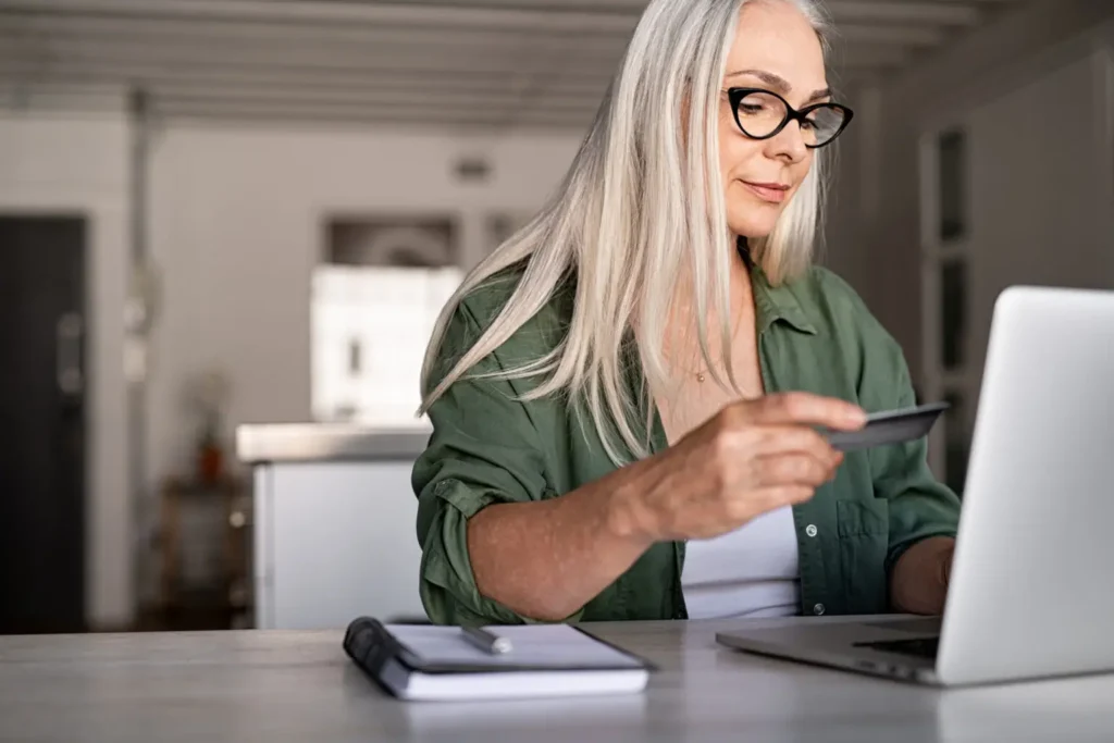 Woman looking at credit card while using laptop