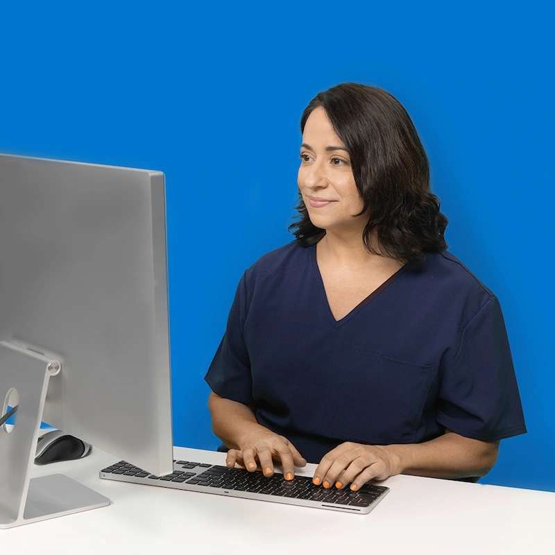 A photo of a female office manager in scrubs typing on a computer.