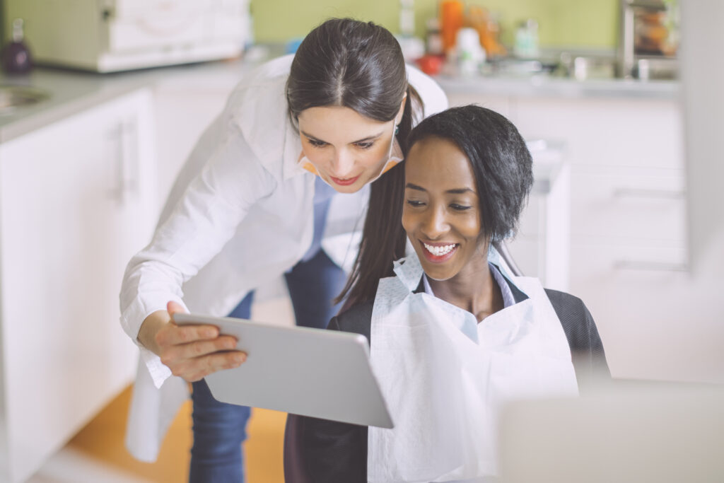 A dentist reviews patient information on a tablet with a patient in a dental chair